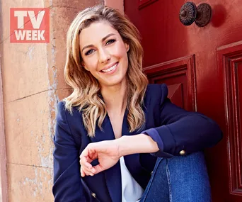 Lou Ransome smiling, sitting casually in jeans and a blazer, against a red door with the TV Week logo in the corner.