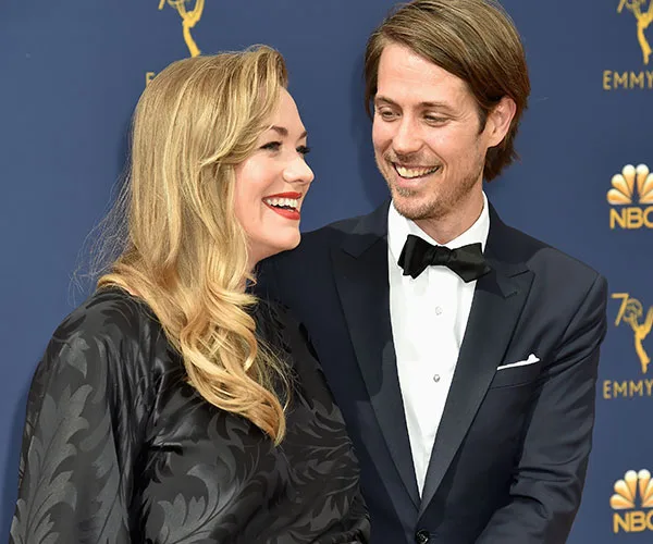 Two people smiling at each other on the red carpet, both dressed in formal attire, with an Emmy Awards backdrop.