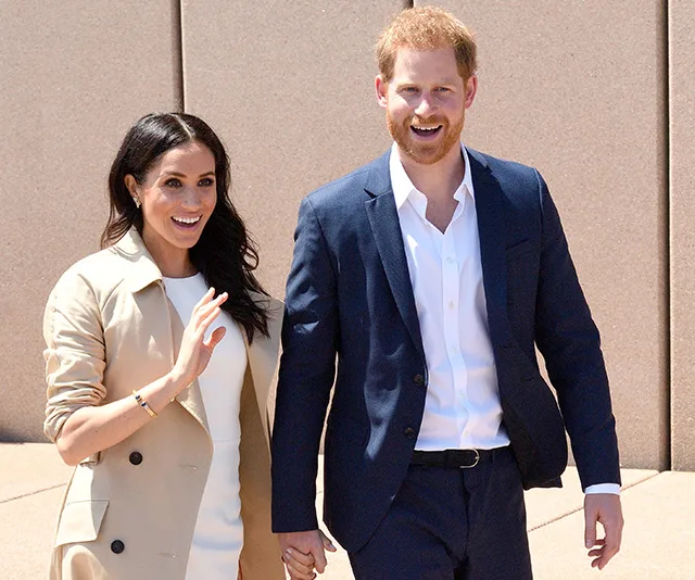 Prince Harry and Meghan Markle smiling and holding hands during a public appearance in Australia.