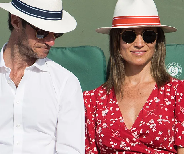 A couple sitting together, wearing sunglasses and hats, with the woman in a red patterned dress.