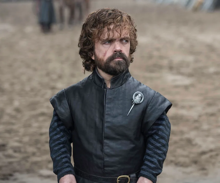 Tyrion Lannister in dark leather, standing on a sandy terrain, wearing a Hand of the King pin.
