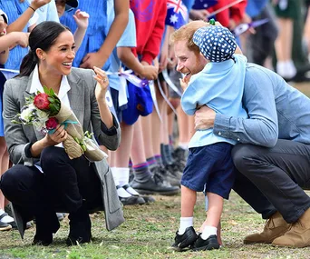 A woman holding flowers kneels while a man hugs a child wearing a hat, surrounded by children in uniforms.
