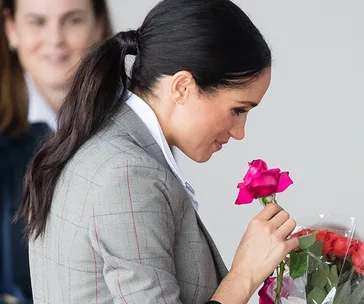 Meghan Markle smelling pink roses, wearing a plaid blazer, during an appearance in Dubbo, Australia.