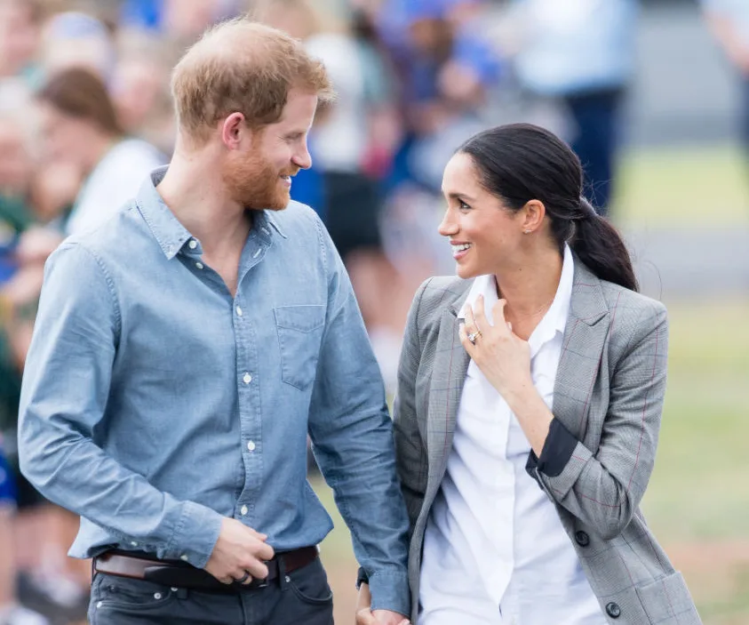 A couple smiling and holding hands, walking outdoors during a public event.