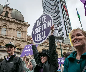 Protesters hold signs advocating for the legalization of abortion in front of a historic building in Queensland.