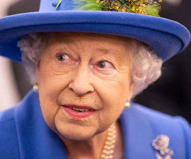 An elderly woman in a blue outfit and hat adorned with colorful decorations, looking to the side.