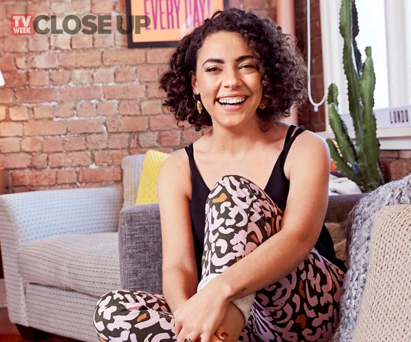 TV Week Close Up feature of a smiling woman with curly hair, wearing a black top and patterned pants, sitting on a couch.