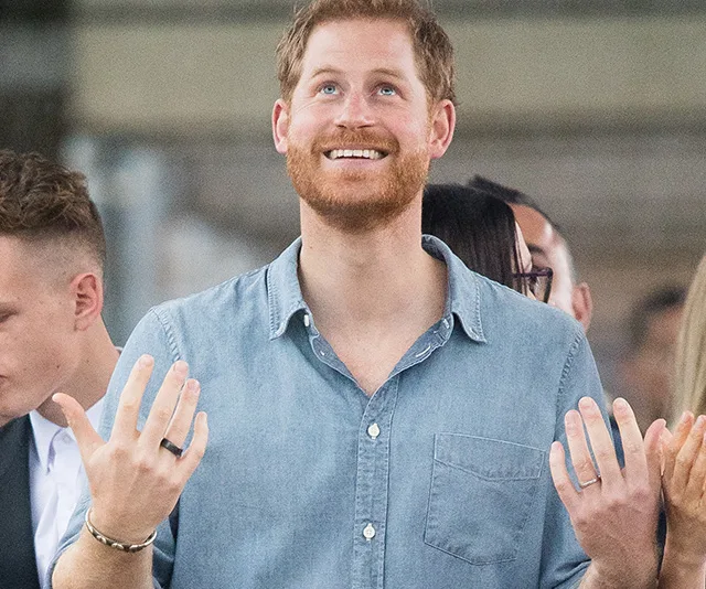 Man smiling and looking up, wearing a denim shirt and bracelets, surrounded by people.