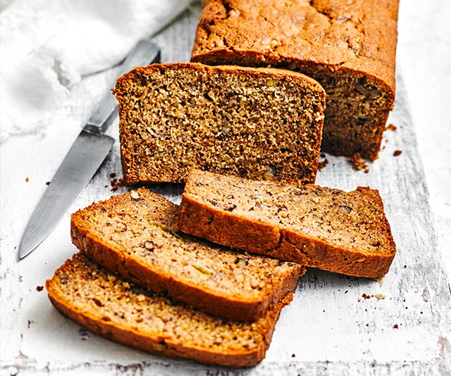 Slices of moist banana bread on a wooden board with a knife.