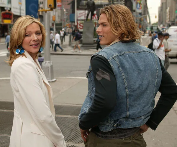 Two people in New York City street scene, turning to look back. One wears a white coat, the other a denim vest.