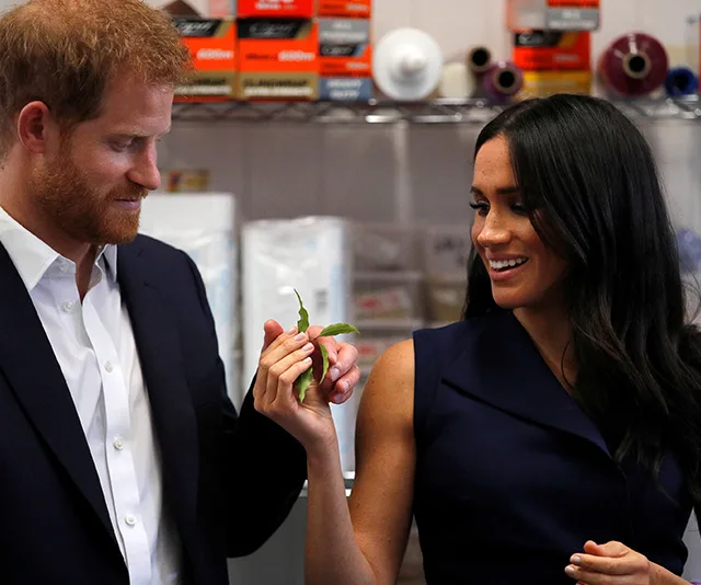 Prince Harry and Meghan Markle hold a vegetable at a Melbourne café, smiling and interacting with each other.