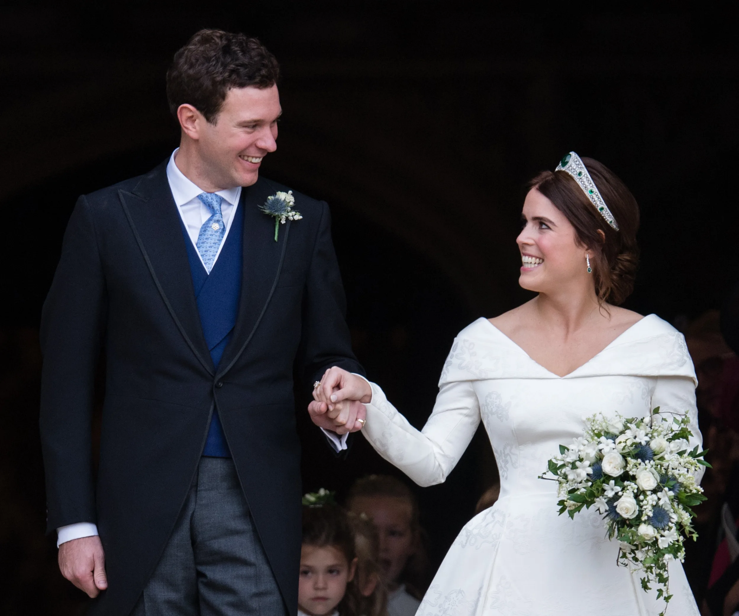 A bride and groom smiling at each other, holding hands; the bride holds a bouquet.