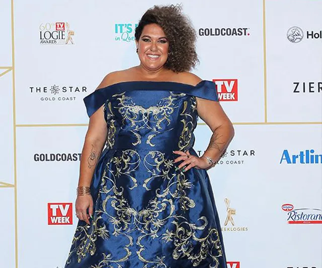 A woman in a blue off-shoulder dress with gold embroidery poses on a red carpet with TV Week and event logos in the background.