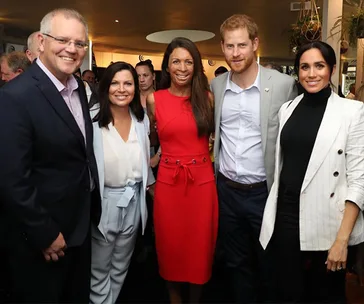 A group of people including Turia Pitt, Prince Harry, and Duchess Meghan smile for a photo at an event.