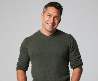 Man in a dark green sweater smiling against a neutral background.