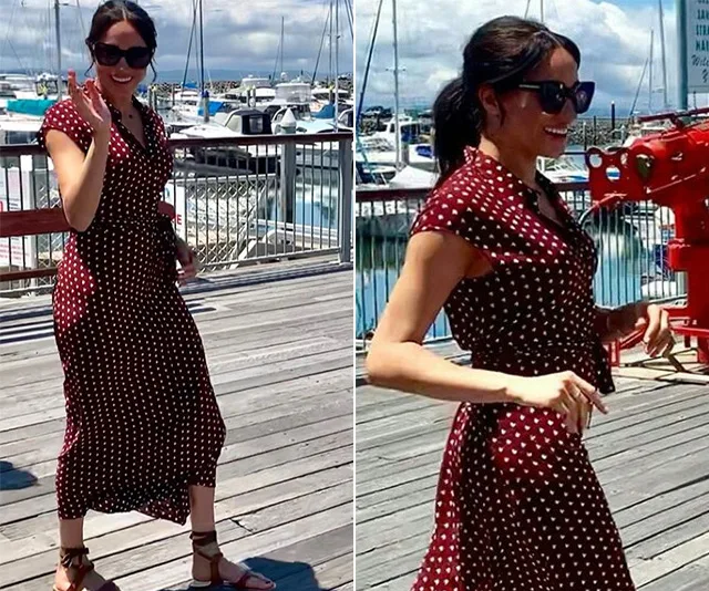Woman in a polka dot dress and sunglasses walking on a sunny marina boardwalk.