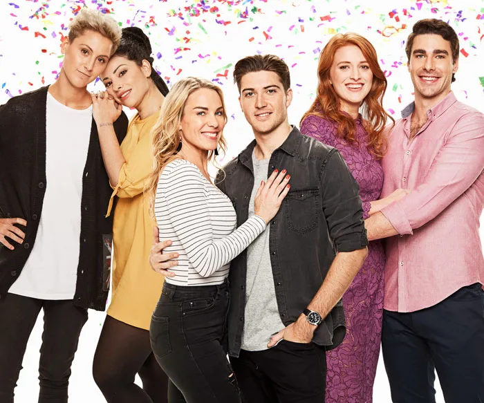 Couples from "Bride and Prejudice" 2018, standing closely in vibrant clothing against a confetti background.
