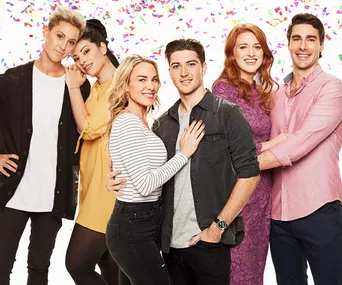 Couples from "Bride and Prejudice" 2018, standing closely in vibrant clothing against a confetti background.