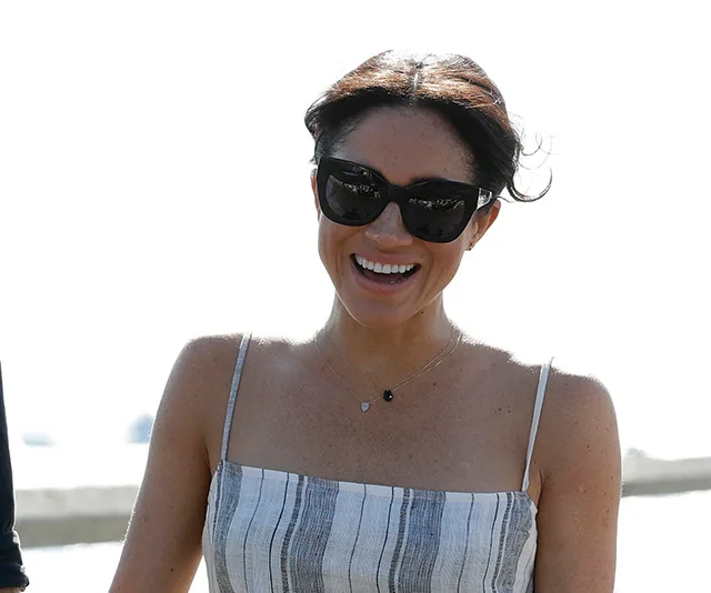 Smiling woman in sunglasses and striped dress stands outdoors on a sunny day.