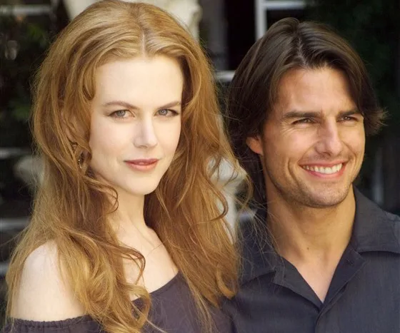 A couple smiling and posing together outdoors, with long hair and casual clothing.