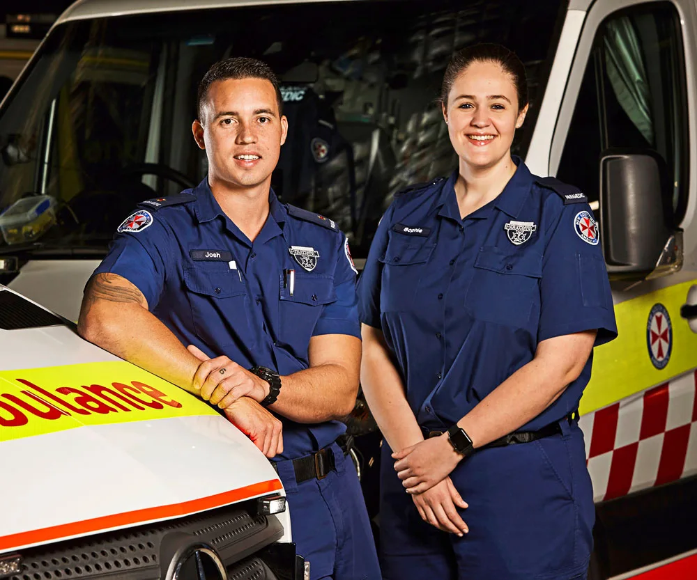 Paramedics in uniform standing in front of an ambulance, smiling confidently.