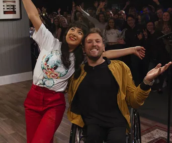 Individuals posing happily in front of a cheering crowd, one seated in a wheelchair.