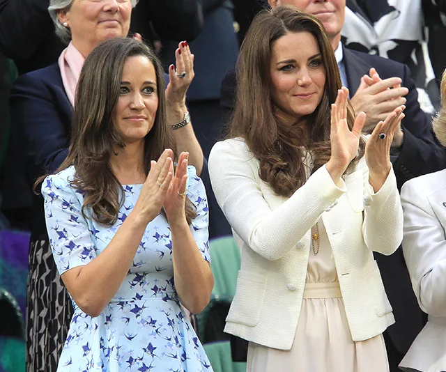 Sisters in dresses and white jacket clapping at an event, surrounded by applauding crowd.