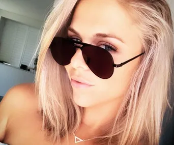 Young woman with blonde hair wearing dark sunglasses indoors.