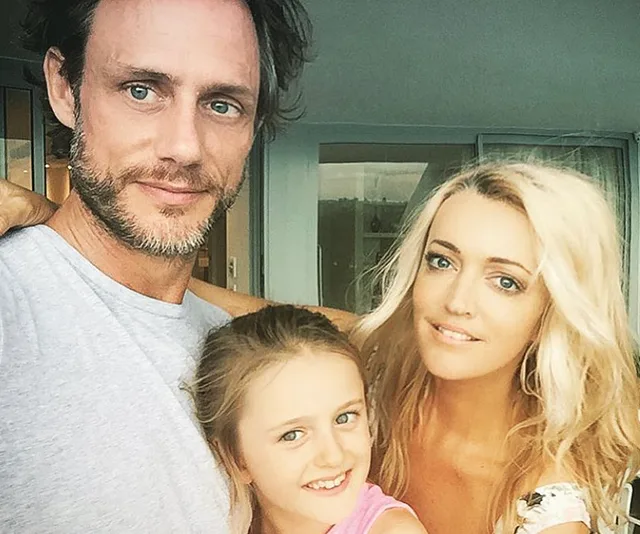 Man, woman, and child smiling together in a casual family photo at home.