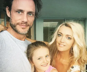 Man, woman, and child smiling together in a casual family photo at home.