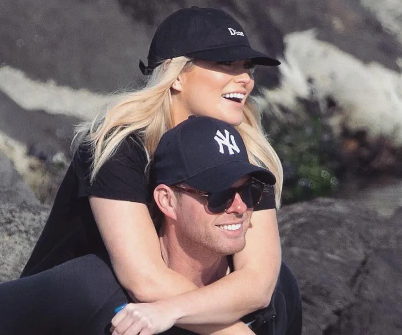 A couple wearing caps enjoying a sunny day outdoors, smiling and embracing each other.