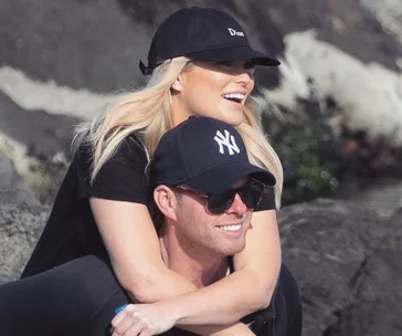 A couple wearing caps enjoying a sunny day outdoors, smiling and embracing each other.