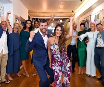 Group of people celebrating with raised fists, dressed in vibrant outfits, smiling in a well-lit room.