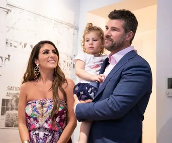 A couple smiling with their child in a home setting, with decorative walls in the background.