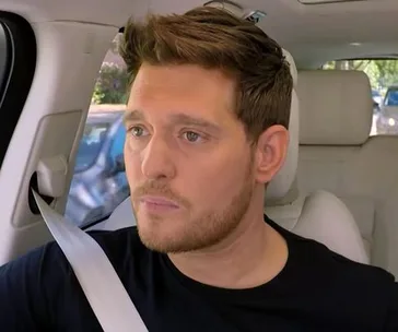 Singer in a car, wearing a black shirt, looking serious, during a Carpool Karaoke segment.