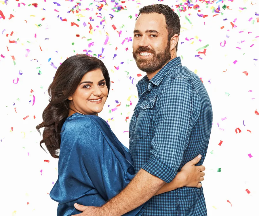 Couple embracing and smiling amidst colorful confetti on a white background.