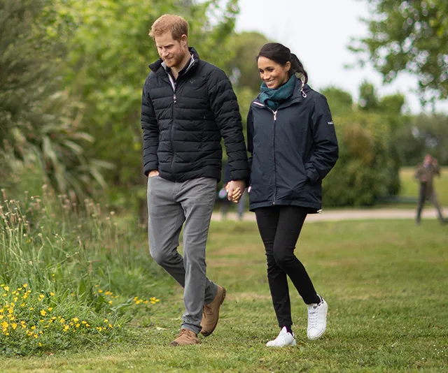 A couple holding hands, walking in a park, surrounded by greenery and flowers.