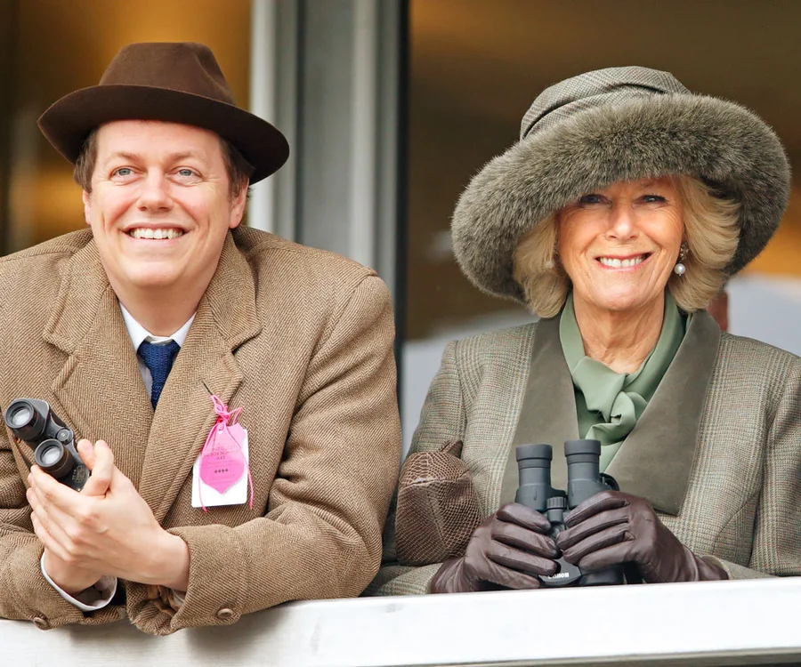 Two people in elegant attire hold binoculars while smiling at an outdoor event.