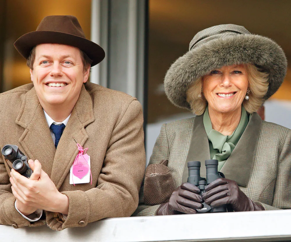 Two people in elegant attire hold binoculars while smiling at an outdoor event.