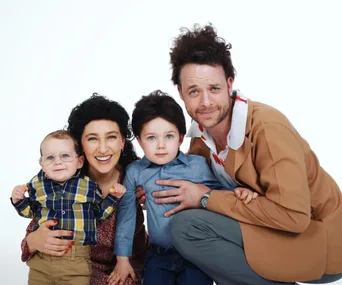 A family dressed in comedy characters' costumes, smiling together, with one adult in a brown jacket and two kids.