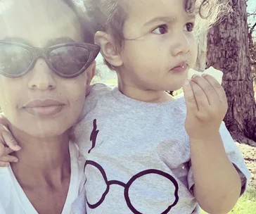 Mother holding toddler outdoors, wearing sunglasses, child in t-shirt with glasses design.