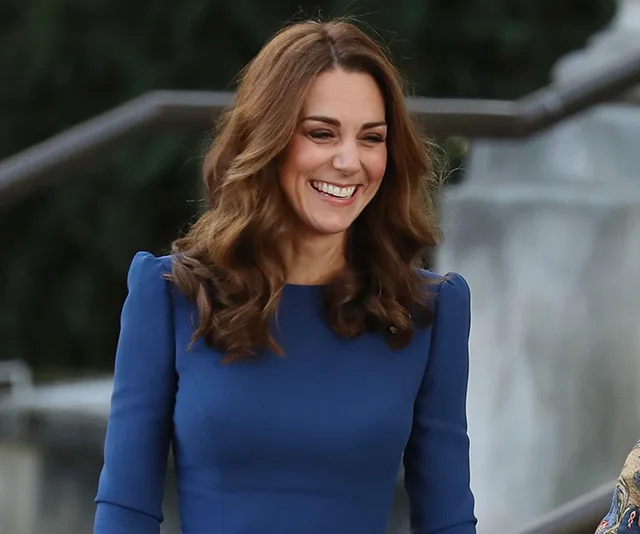 A woman in a blue dress smiling outdoors, near a war museum.