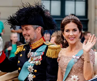 Crown Princess Mary and Crown Prince Frederik of Denmark wave during a formal event, dressed in royal attire.