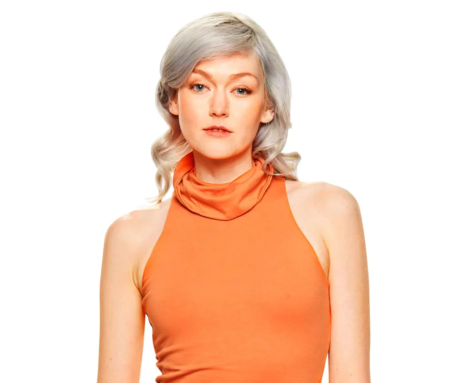 A woman with light hair in an orange sleeveless top poses against a white background.