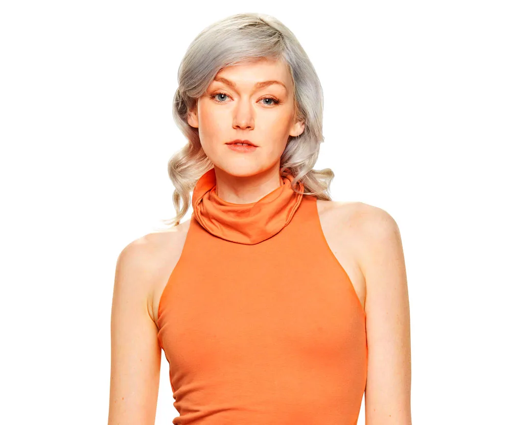 A woman with light hair in an orange sleeveless top poses against a white background.