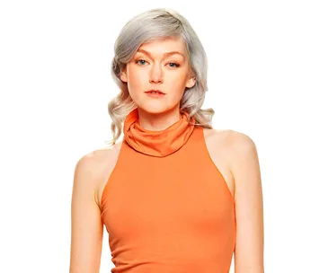 A woman with light hair in an orange sleeveless top poses against a white background.