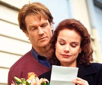 A man with flowers looks over a woman's shoulder as she reads a letter, likely a scene from "SeaChange" reboot.