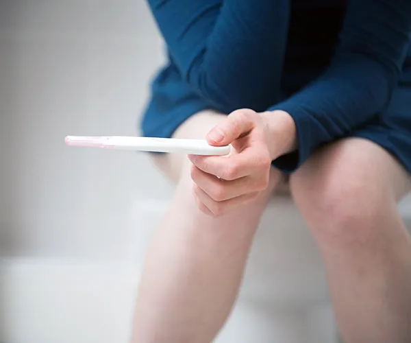 Person in blue clothing holding a pregnancy test while seated.