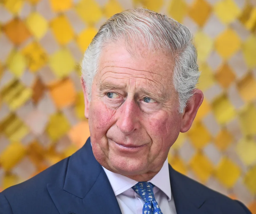 Man in a suit and blue tie, looking to the side, with a yellow patterned background.