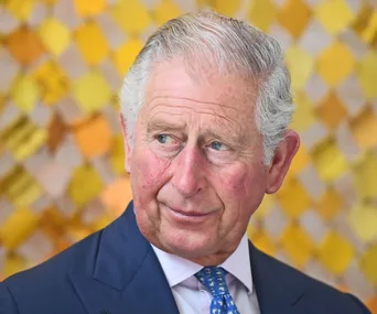 Man in a suit and blue tie, looking to the side, with a yellow patterned background.